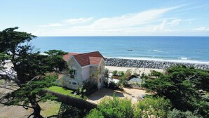 Ein Haus aus Stein mit rotem Dach, ein Strand mit felsigem Ufer und einem strahlend blauen Himmel.