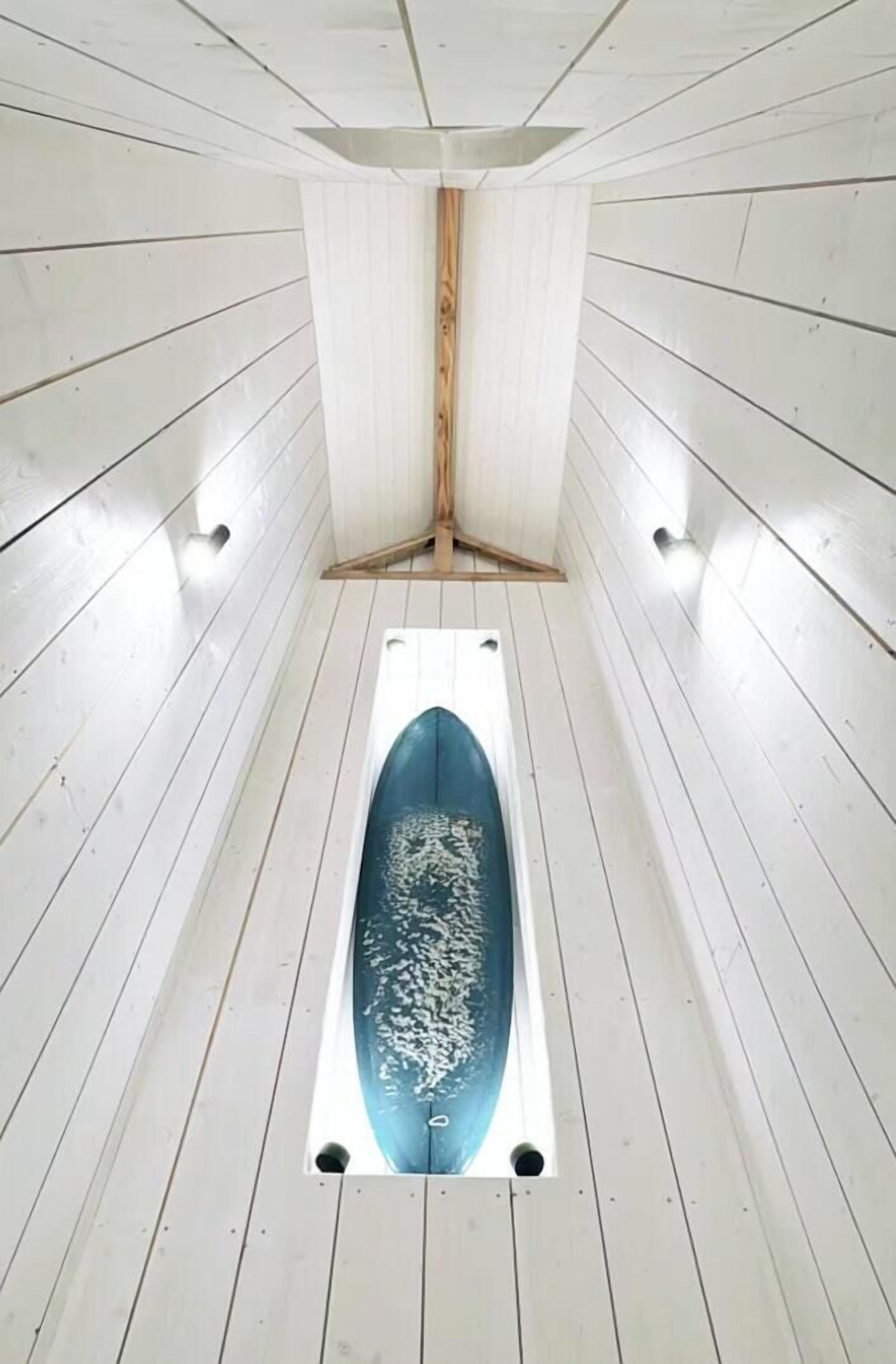 Ein schmaler, länglicher Raum mit weißen Holzwänden und einer blauen Badewanne in der Mitte.