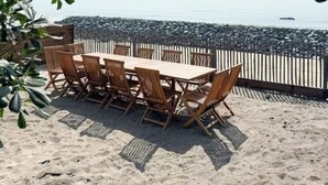 Ein Holztisch mit Stühlen steht auf einem Sandstrand mit Blick aufs Meer.