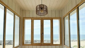 Ein Zimmer mit Holzwänden und -bänken, große Fenster mit Blick auf Strand und Meer.