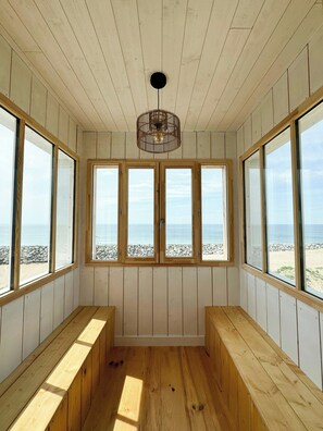 Ein Zimmer mit Holzwänden und -bänken, große Fenster mit Blick auf Strand und Meer.