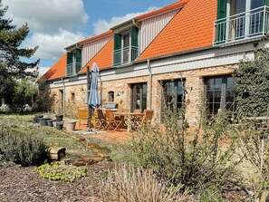 Ein zweistöckiges Steinhaus mit rotem Ziegeldach, Außenbestuhlung und einem Garten.