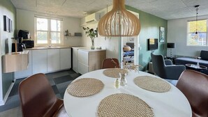 A modern kitchen with white cabinets, a dining table with woven placemats, and a hanging light fixture. - Relax in the countryside with pool (Aulum)