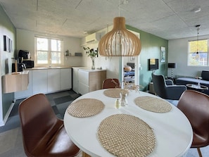 A modern kitchen with white cabinets, a dining table with woven placemats, and a hanging light fixture. - Relax in the countryside with pool (Aulum)