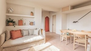 Ein moderner Wohnraum mit einer Couch, einem Esstisch, Stühlen, einem Regal mit Dekoration und einer Tür zu einem anderen Raum.