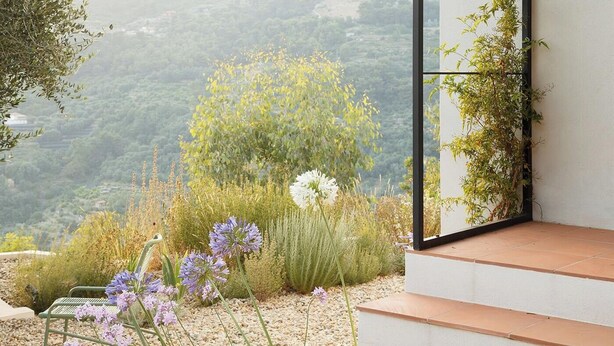 Ein moderner Außenbereich mit Blick auf eine hügelige Landschaft, einer Metallbank und einer Treppe, die zu einer Glastür führt.