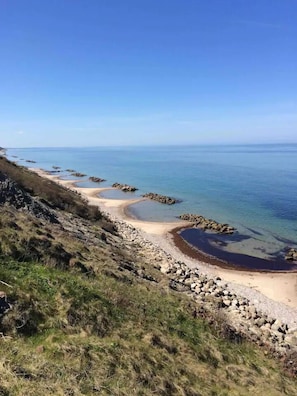 A coastal landscape with a sandy beach, rocky outcrops, and clear blue water. - The small, red wooden house with lots of charm (Vejby Strand)