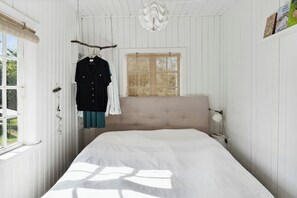 A bedroom with a bed, a window with a view, a hanging coat rack, and a wall-mounted lamp. - The small, red wooden house with lots of charm (Vejby Strand)