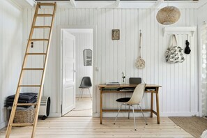 A room with a wooden ladder, a desk with a chair, a wicker basket, and a door leading to another room. - The small, red wooden house with lots of charm (Vejby Strand)