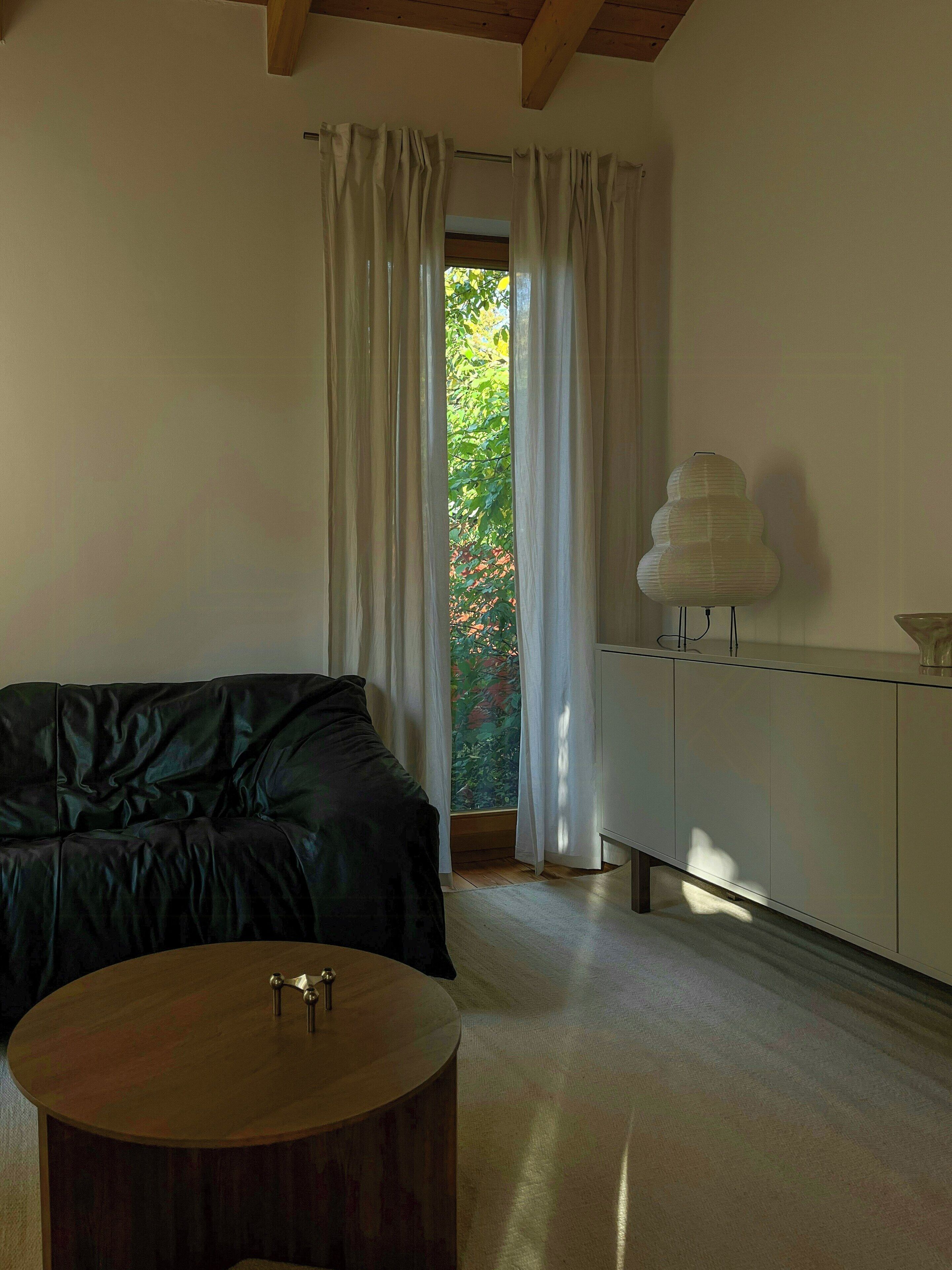 A modern room with a black leather sofa, a wooden side table, a white cabinet, and a view of greenery outside.