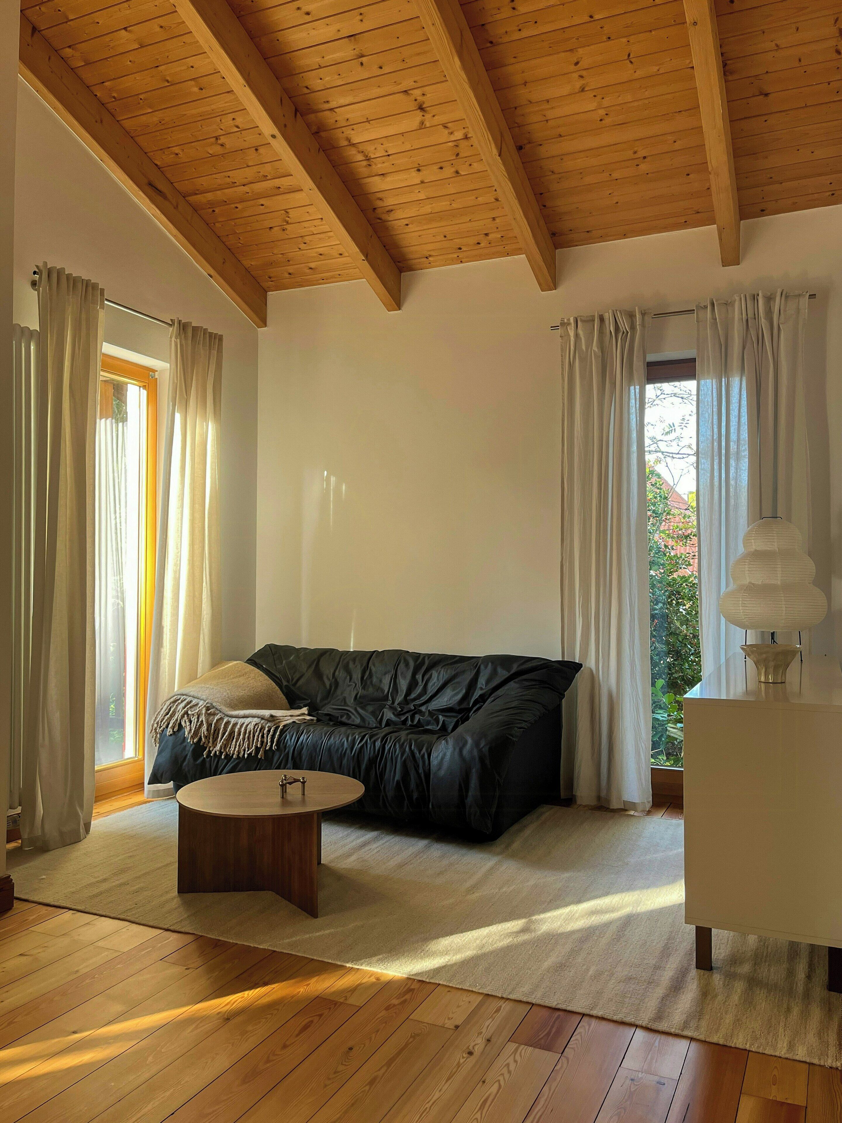 Ein Zimmer mit Holzboden, einer schwarzen Ledercouch, einem runden Holztisch und einem weißen Schrank.