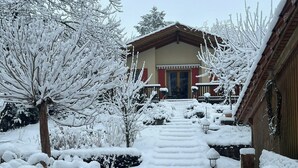 Ein verschneiter Weg führt zu einem Gebäude mit Holzfassade und roter Tür.
