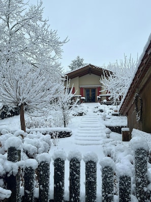 Un sendero cubierto de nieve que conduce a un edificio con fachada de madera y puerta roja.