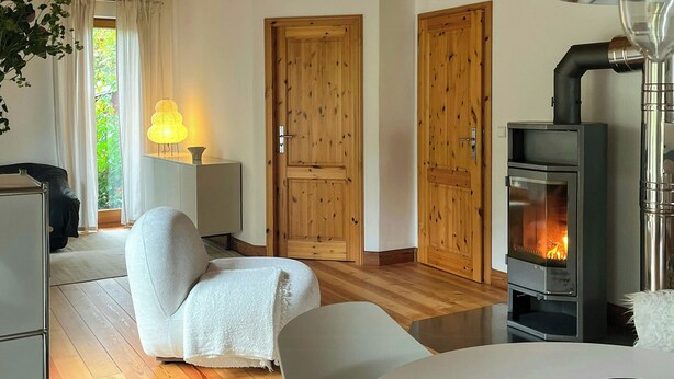 Ein gemütlicher Raum mit Holzbalkendecke, einem weißen Sofa, einem Tisch mit einer Banane und einem Kaminofen.