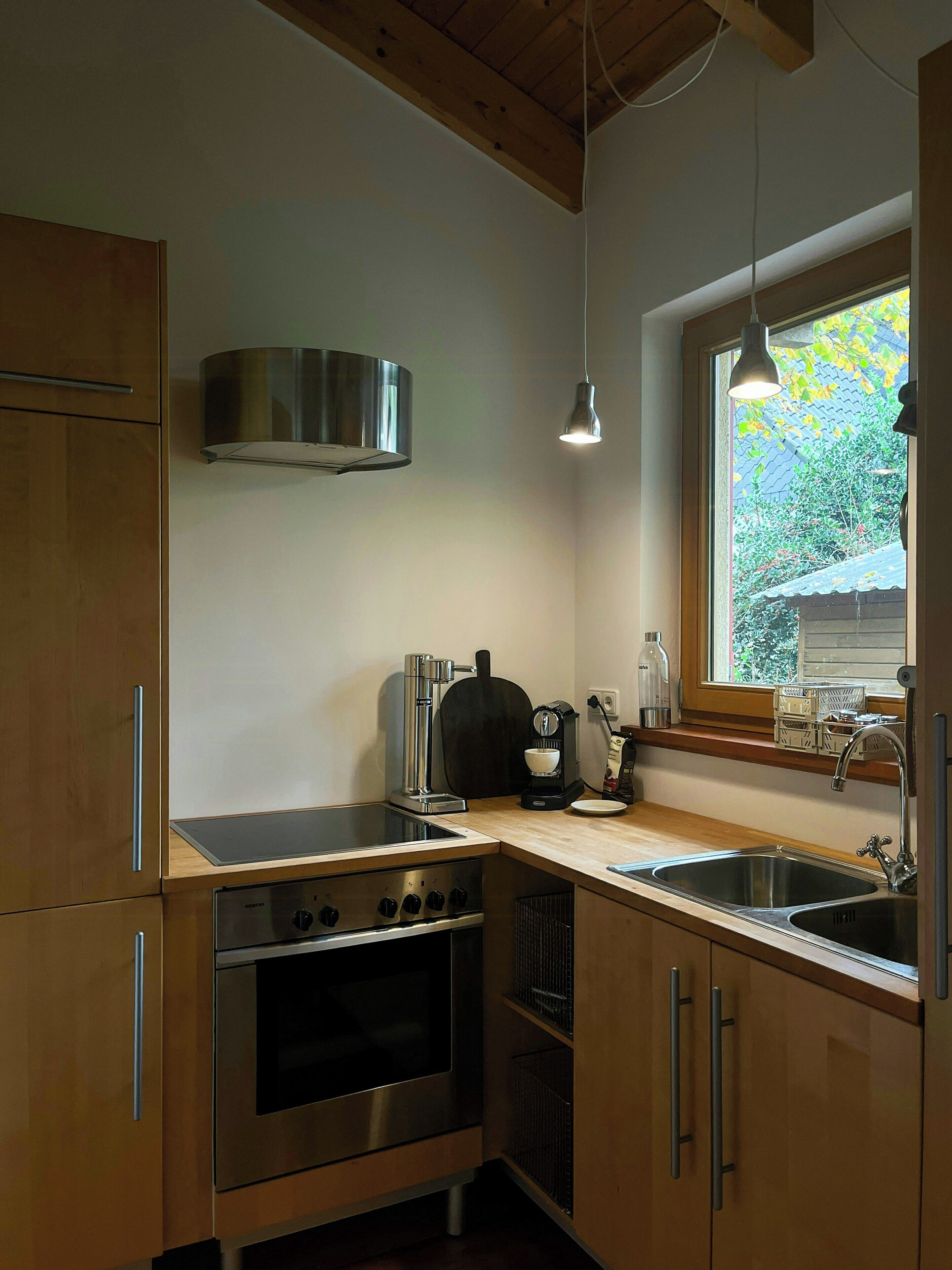 Eine moderne Küche mit Holzausstattung, Edelstahlgeräten, einem Einbauofen, einer Kaffeemaschine und einem Fenster mit Blick auf Grünflächen.