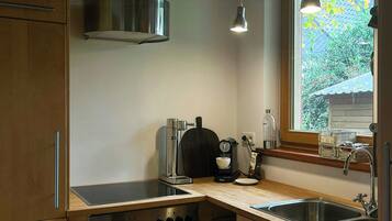Eine moderne Küche mit Holzausstattung, Edelstahlgeräten, einem Einbauofen, einer Kaffeemaschine und einem Fenster mit Blick auf Grünflächen.