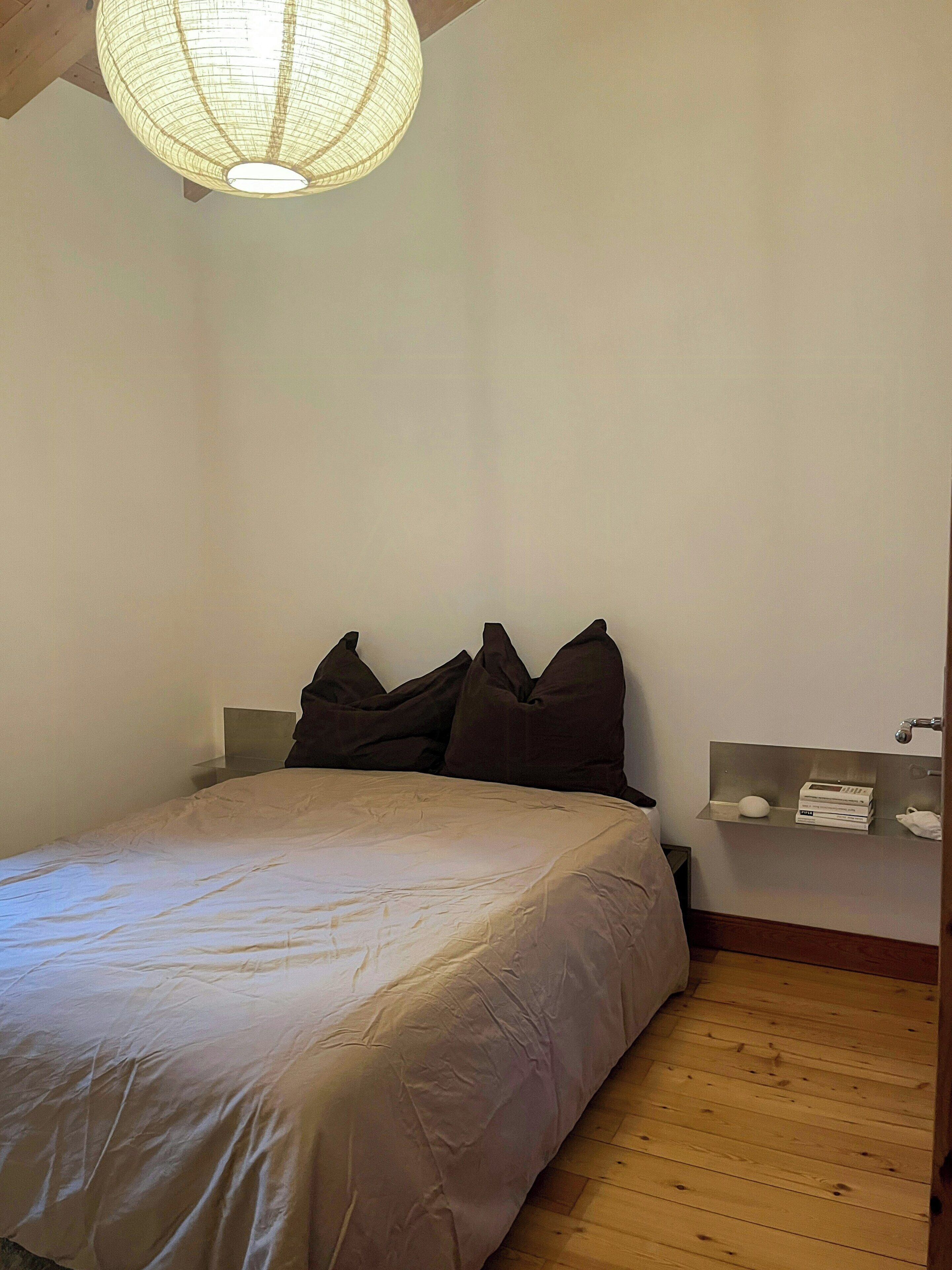 Ein Schlafzimmer mit Bett, Kissen, einem Nachttisch, einer Ablage und einer Pendelleuchte.