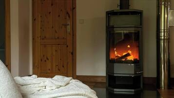 Ein Zimmer mit Kaminofen, Holztür und einer Couch mit weißer Decke.