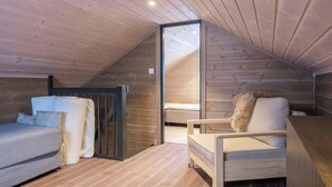 Dormitorio tipo loft con techo inclinado, paredes de madera, una cama, una silla y un escritorio pequeño.