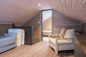 Ein Schlafzimmer im Loft-Stil mit schrägem Dach, Holzwänden, einem Bett, einem Sessel und einem kleinen Schreibtisch.
