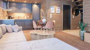 Un interior moderno con techo de madera, una zona de comedor con sillas rosadas, un sofá y una cocina con armarios grises.
