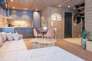 Ein modernes Interieur mit Holzbalkendecke, einem Essbereich mit rosafarbenen Stühlen, einer Couch und einer Küche mit grauen Schränken.