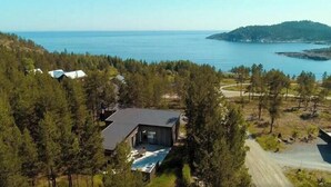 A modern house with a large deck overlooking a lake, surrounded by dense forest.