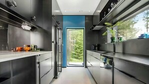 A modern kitchen with stainless steel appliances, a blue accent wall, and a view of a forest through a large window.