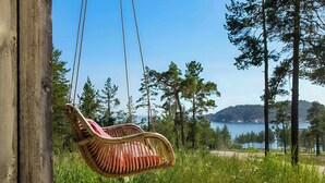 A wooden swing chair hanging from a wooden post, overlooking a forest and a body of water.