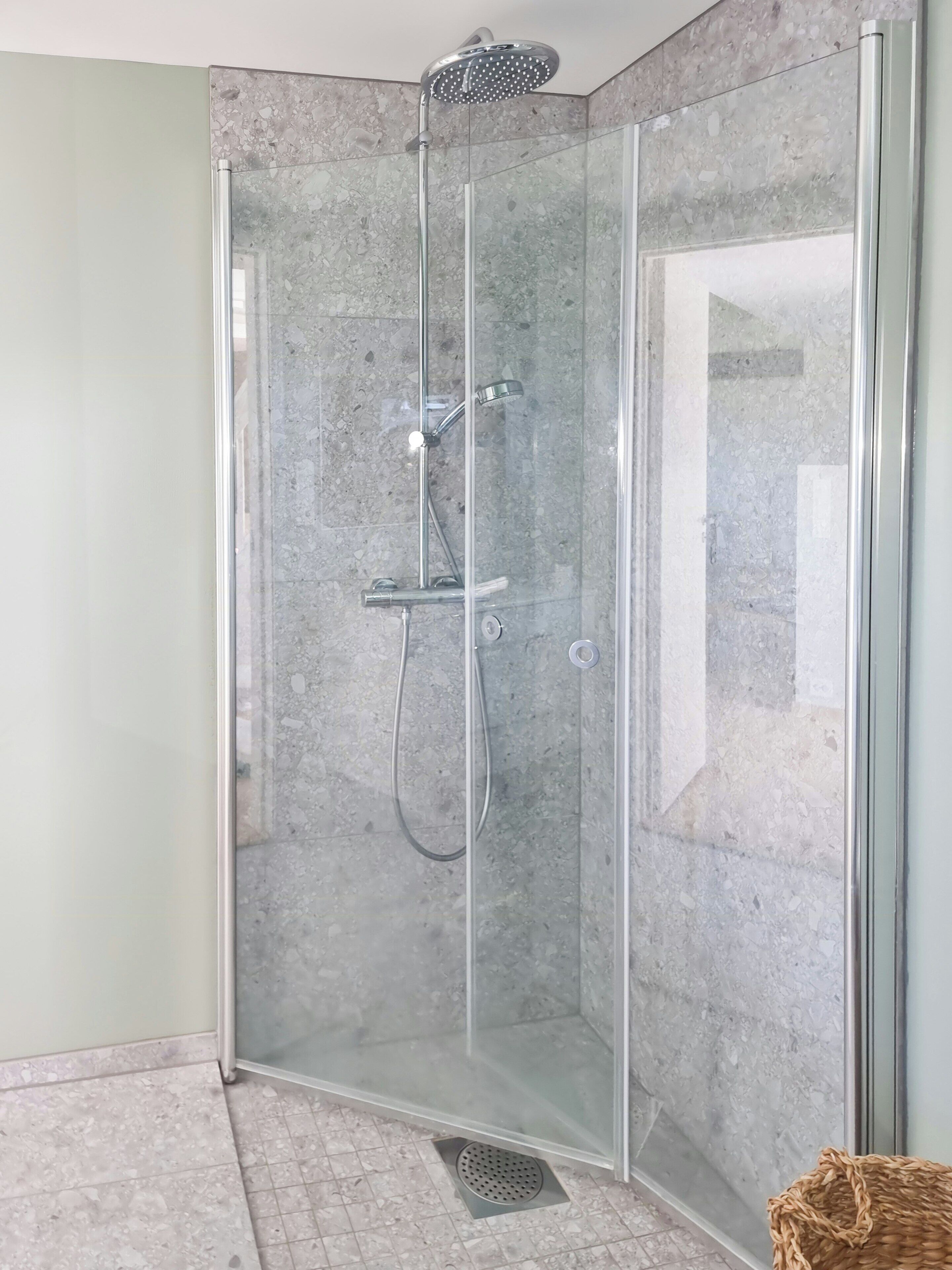 A glass-enclosed shower with a handheld showerhead and a handheld faucet.
