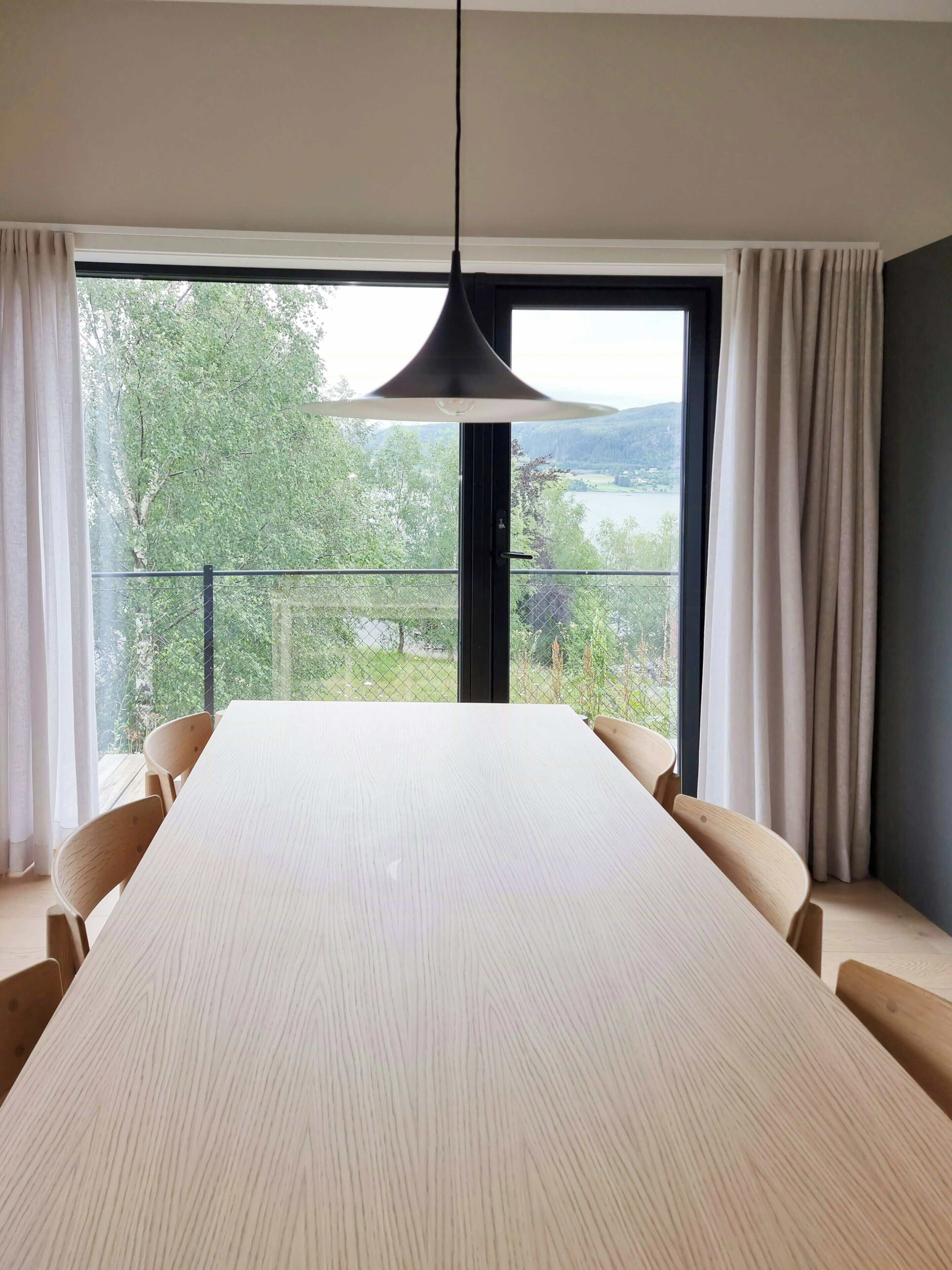 Un comedor moderno con una mesa grande, sillas, una lámpara colgante y vistas a través de un ventanal.