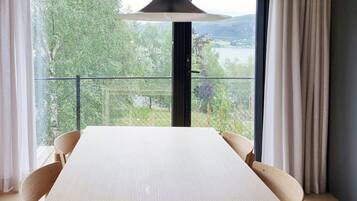 Un comedor moderno con una mesa grande, sillas, una lámpara colgante y vistas a través de un ventanal.