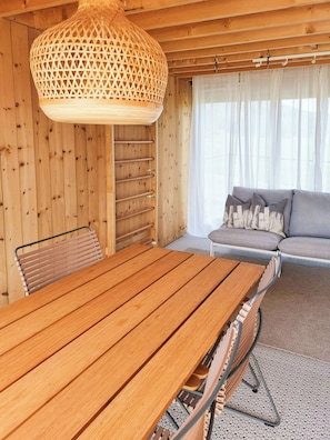 A wooden interior with a dining table, chairs, a sofa, and a hanging light fixture.