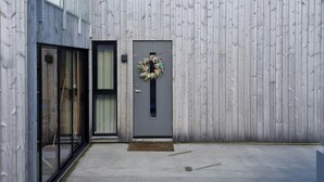A modern building with a wooden facade, a grey door with a wreath, and a concrete courtyard. - Cabin by the fjord with rooftop terrace on Randøy (Hjelmeland)