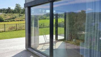 A modern building with large glass windows, a wooden deck, and a view of a green landscape.