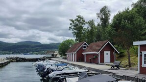 A marina with boats docked, a row of small buildings, and a body of water with mountains in the background. - Cabin by the fjord with rooftop terrace on Randøy (Hjelmeland)