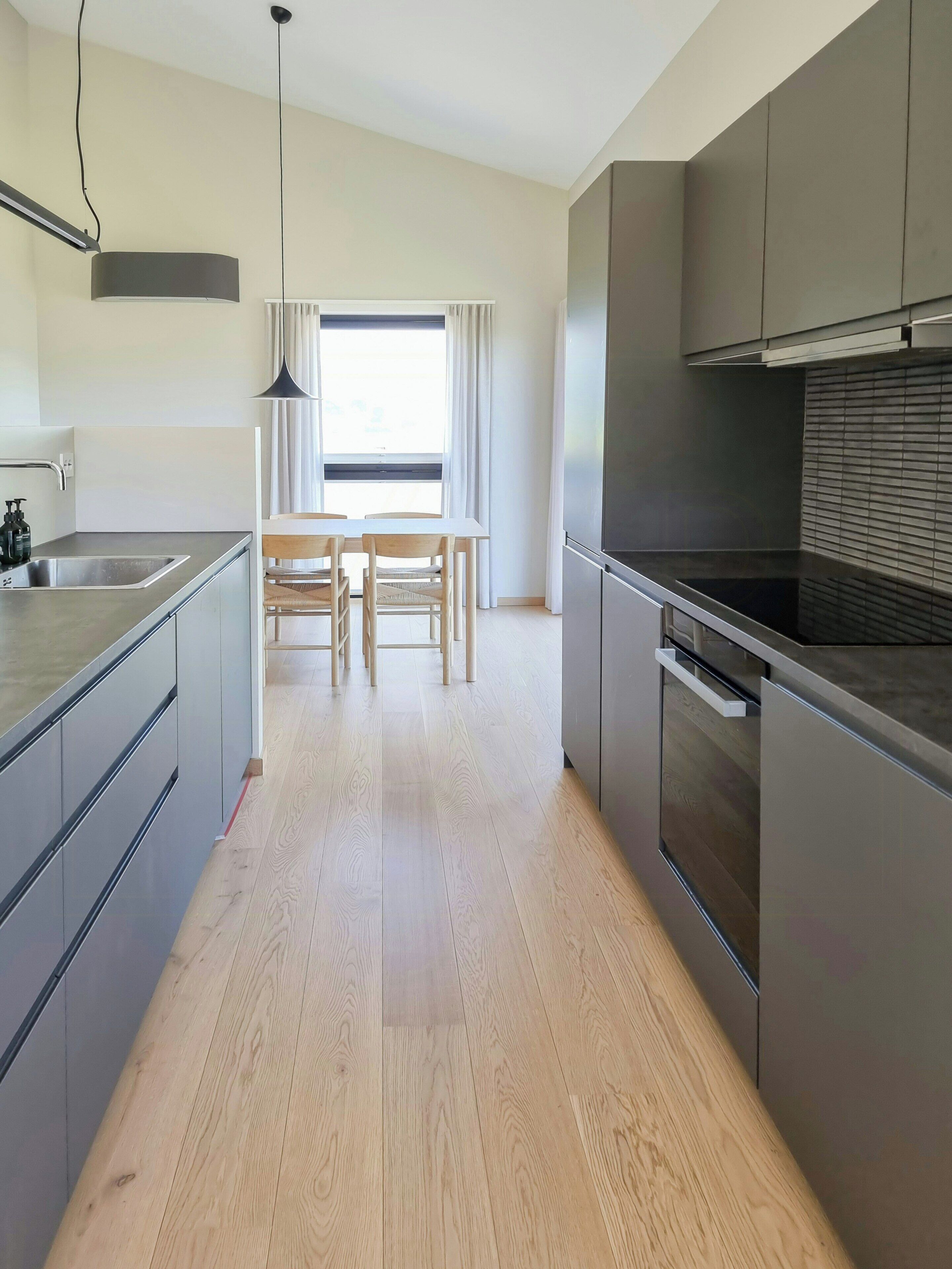 Een moderne keuken met een centraal eiland, een eetgedeelte met tafel en stoelen, en een groot raam met gordijnen.