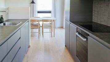 Een moderne keuken met een centraal eiland, een eetgedeelte met tafel en stoelen, en een groot raam met gordijnen.