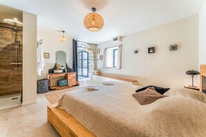 Ein Schlafzimmer mit einem großen Bett, einer hölzernen Bank, einem Schminktisch und einem Spiegel, sowie einer Treppe, die zu einem Außenbereich führt.
