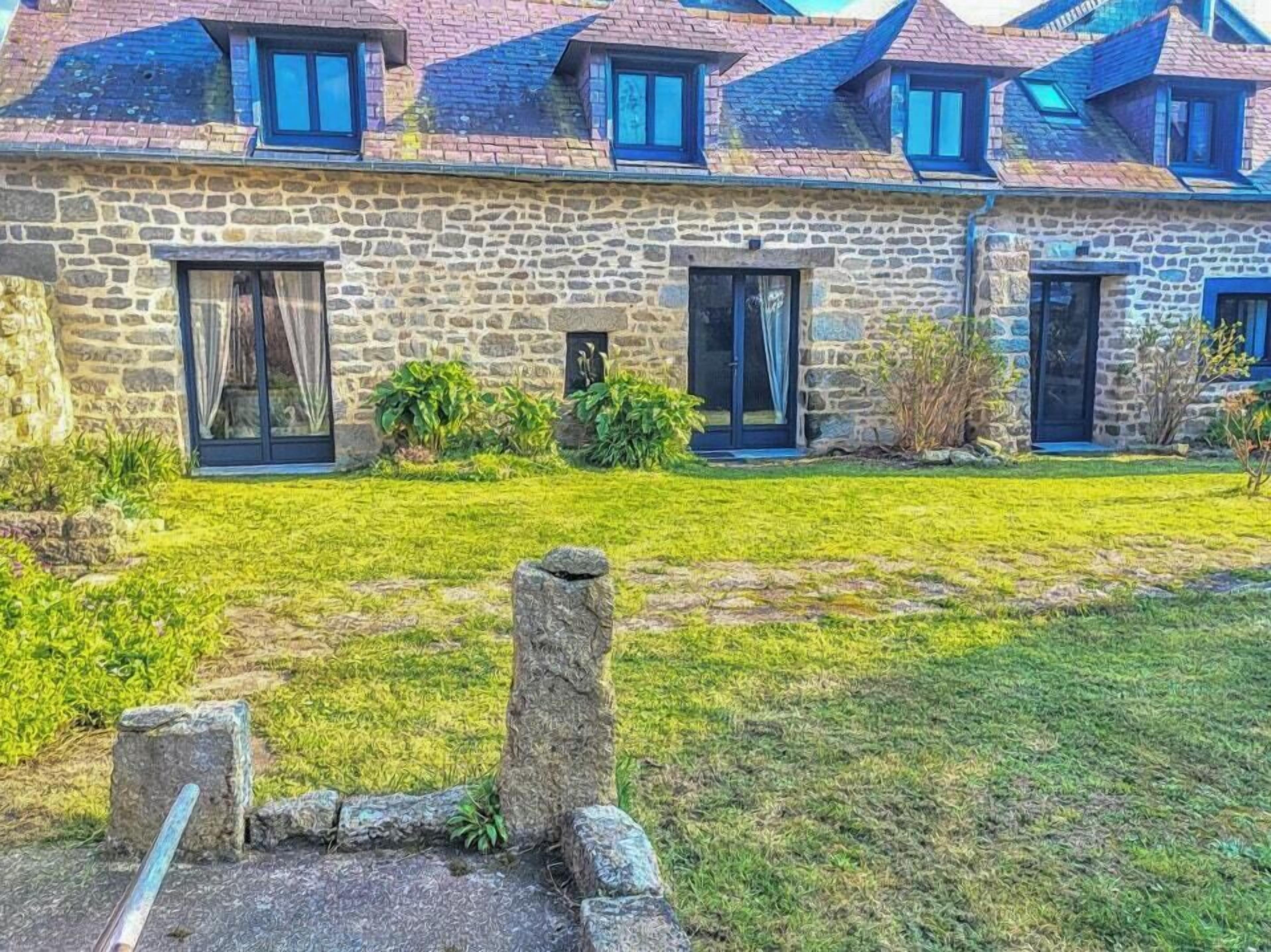 A stone building with multiple windows and doors, a grassy yard, and a stone wall.