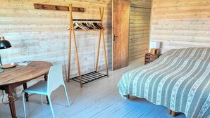 Ein Zimmer in einer Holzhütte mit einem Bett, einem Tisch mit Stuhl und einem Kleiderständer.
