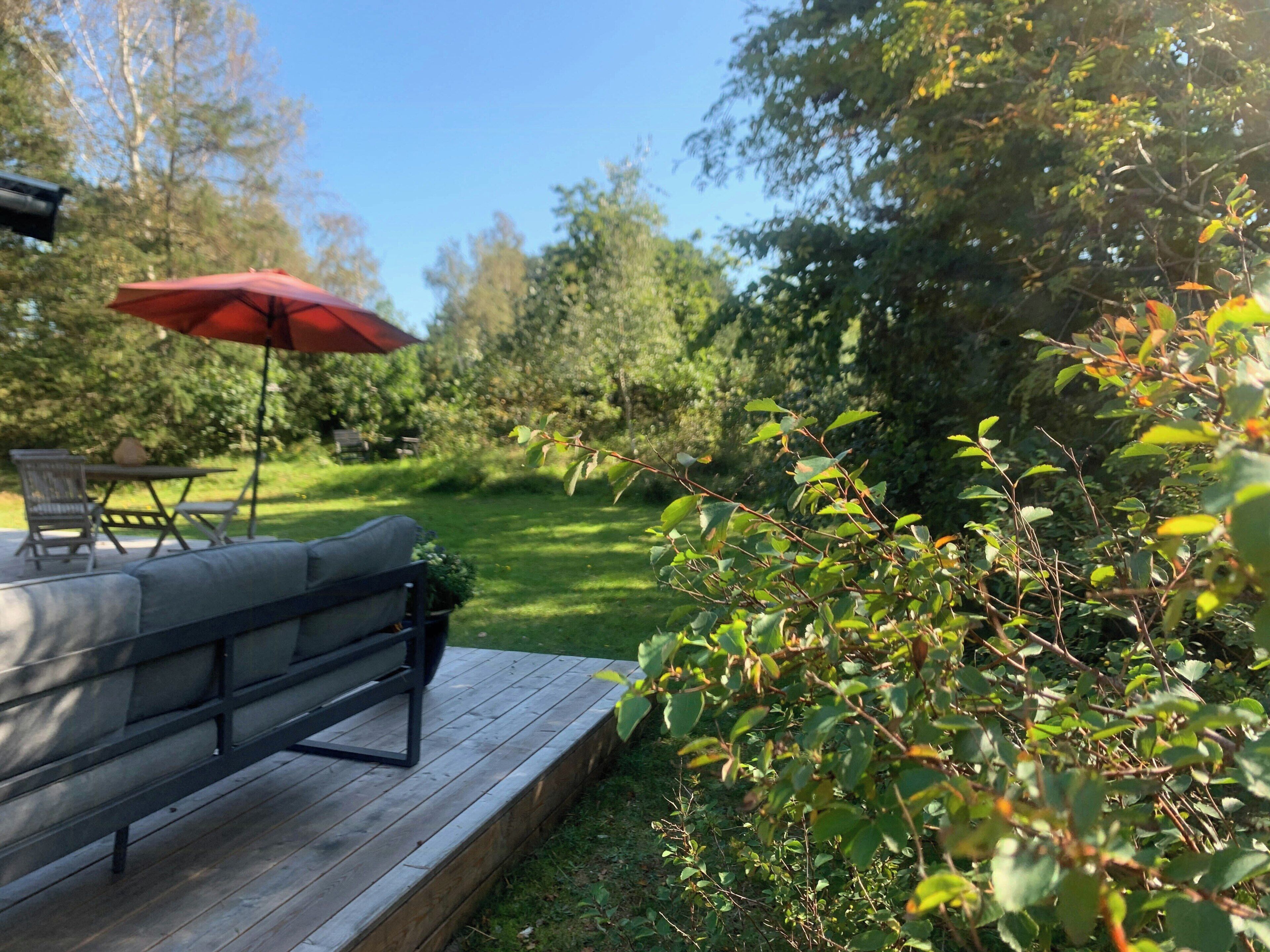 A deck with a grill, outdoor furniture, and a red umbrella.