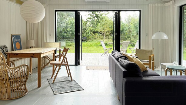 Um interior moderno com área de refeições, sofá e grandes portas de vidro deslizantes que dão para um jardim.