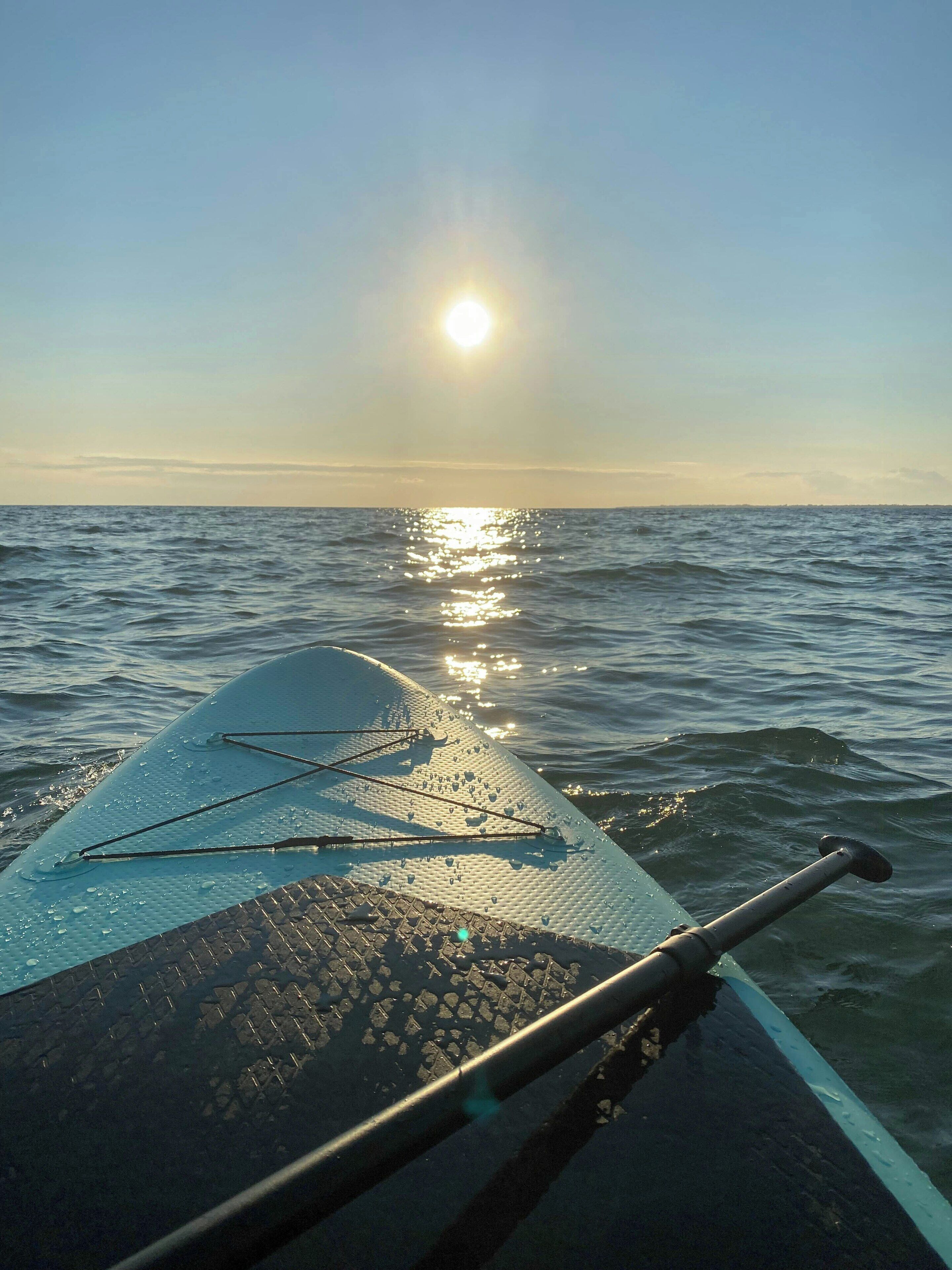 La prua di una barca con la scia nell'acqua, cielo sereno e il sole che si riflette sulla superficie.