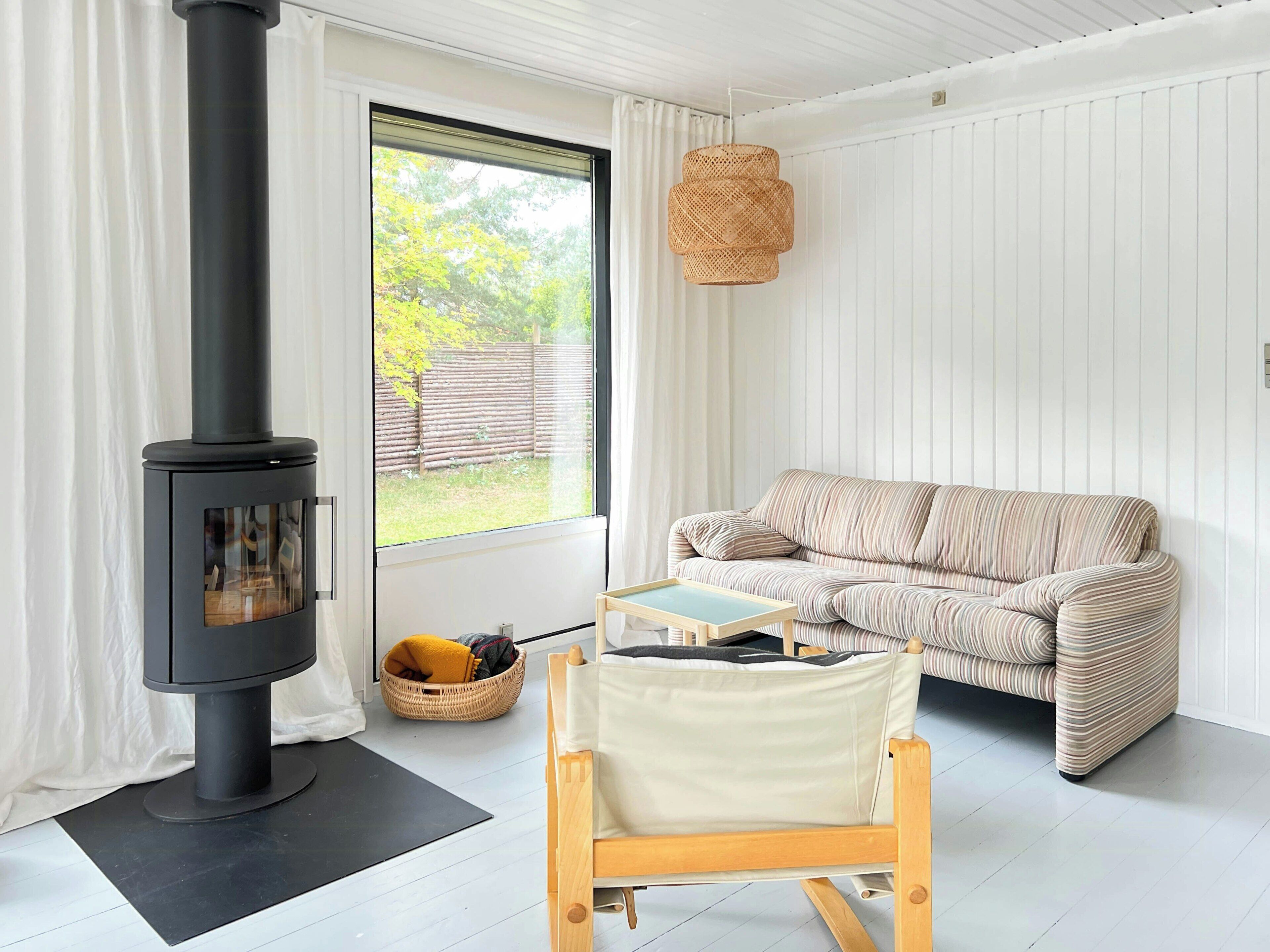 Un salon chaleureux avec un poêle à bois noir, un canapé à rayures, une chaise en bois et un panier en osier.