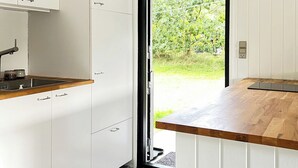 Uma cozinha moderna com armários brancos, bancada de madeira e vista para o verde lá fora.