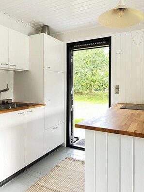 A modern kitchen with white cabinets, a wooden countertop, and a view of greenery outside. - Home embraced by green nature in Højby (Højby)