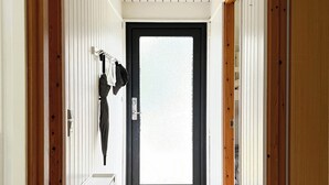 Um corredor com uma porta no fim, um cabideiro com um casaco e um aparador branco.
