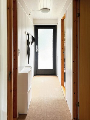 A hallway with a door at the end, a coat rack with a jacket, and a white dresser. - Home embraced by green nature in Højby (Højby)