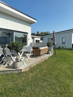 Ein modernes Haus mit Terrasse, Gartenmöbeln und einem kleinen Baum.
